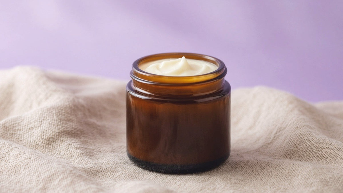 Amber glass jar of handmade tallow balm on linen with soft lavender light
